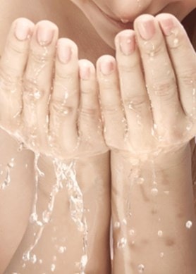 Frau mit langen Haaren wäscht sich das Gesicht mit Wasser
